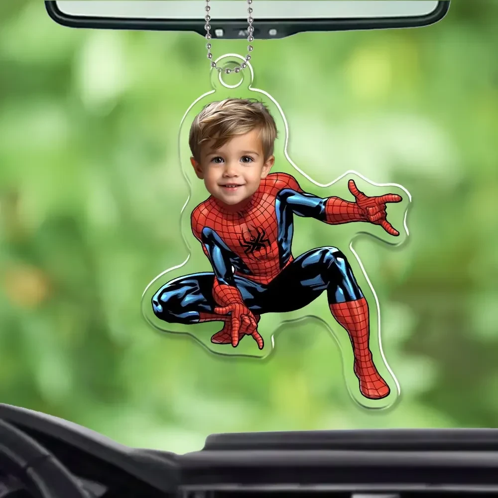 Close-up of a custom die-cut acrylic car charm with a personalized superhero photo design against a blurred outdoor background
