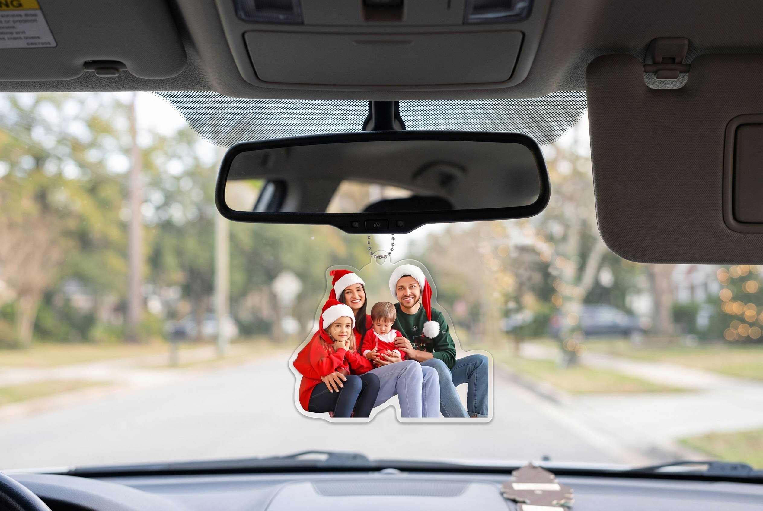 Custom personalized car rearview mirror charm with a die-cut family Christmas photo of a couple and two children wearing Santa hats, hanging from a metal ball chain inside a car interior