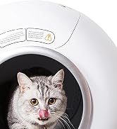 White, spherical pet device with a circular opening. Inside, a gray tabby cat is visible, licking its nose. Warning labels are visible on the top of the device.